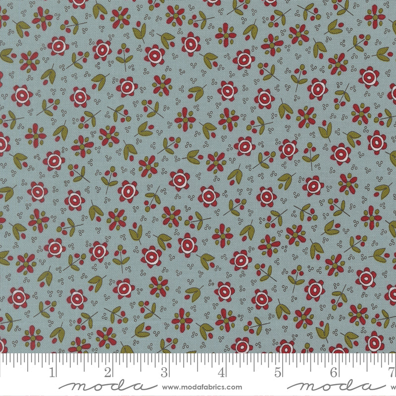 A close-up of a fabric pattern featuring small red and white flowers with green leaves on a muted blue-gray background, with a ruler along the bottom edge.