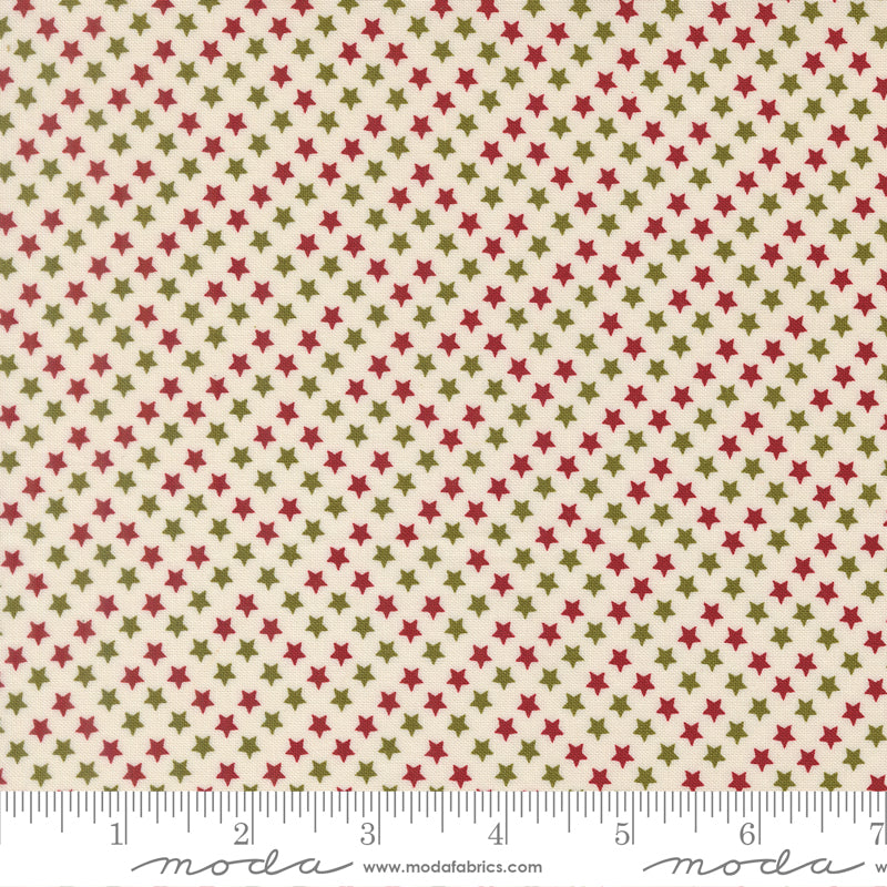 A close-up of a fabric pattern featuring small red and olive green stars on a warm cream background, with a ruler along the bottom edge showing scale.