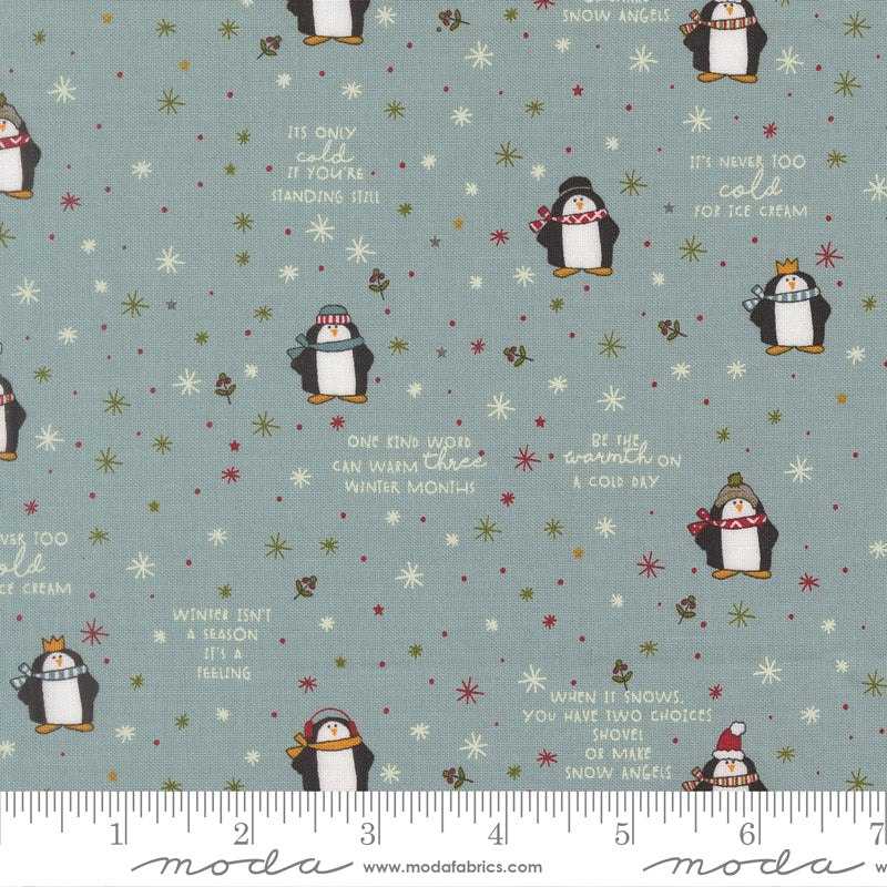 A fabric pattern swatch featuring penguins and winter quotes on a dusty blue-gray background, with a measuring ruler at the bottom showing scale.