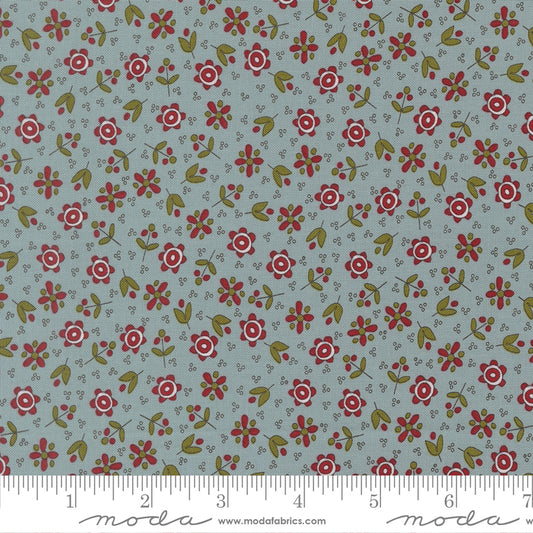 A close-up of a fabric pattern featuring small red and white flowers with green leaves on a muted blue-gray background, with a ruler  along the bottom edge.