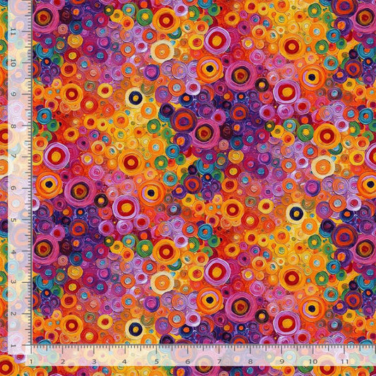 A close-up of a colorful abstract fabric or wallpaper pattern featuring concentric circles and dots in orange, yellow, purple, pink, blue, green, and red, with a ruler along the left and bottom edges showing scale.