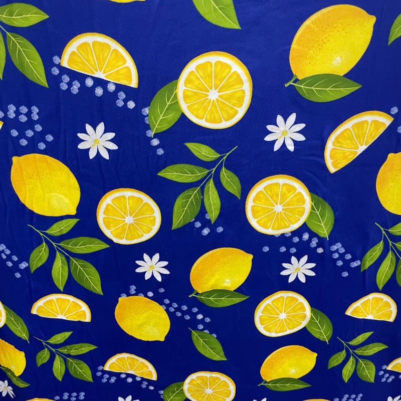 A close-up of a blue fabric with a repeating pattern of yellow lemons, green leaves, and small white flowers.